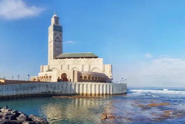 The towering minaret of the Hassan II Mosque, a prominent tourist spot and the architectural landmark of Casablanca, Morocco, standing tall against the skyline by the sea.